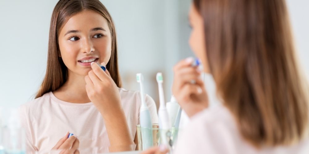 A young girl applying lip balm min the mirror