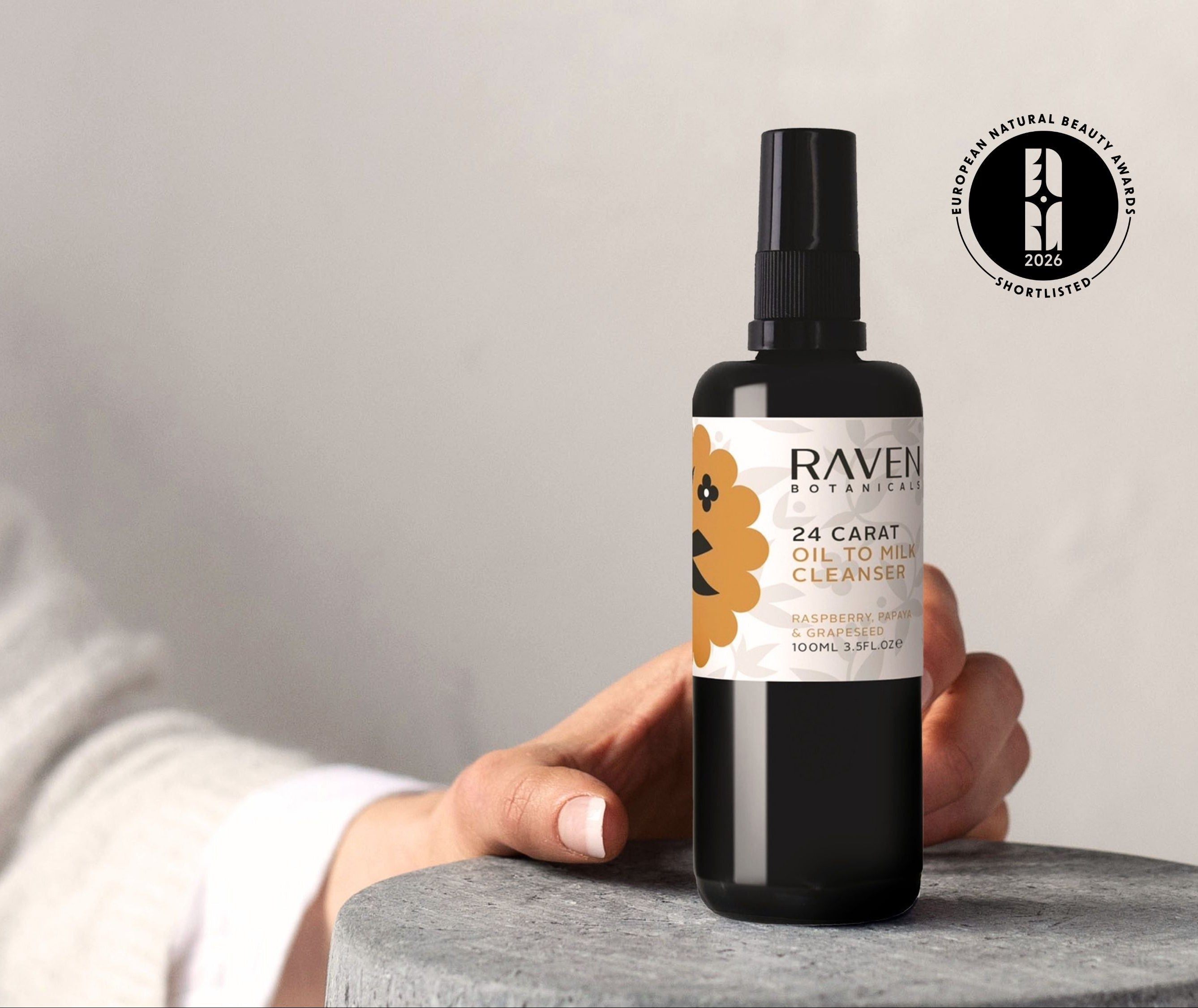 Bottle of RAVEN skin care product held by a person on a stone surface with a neutral background