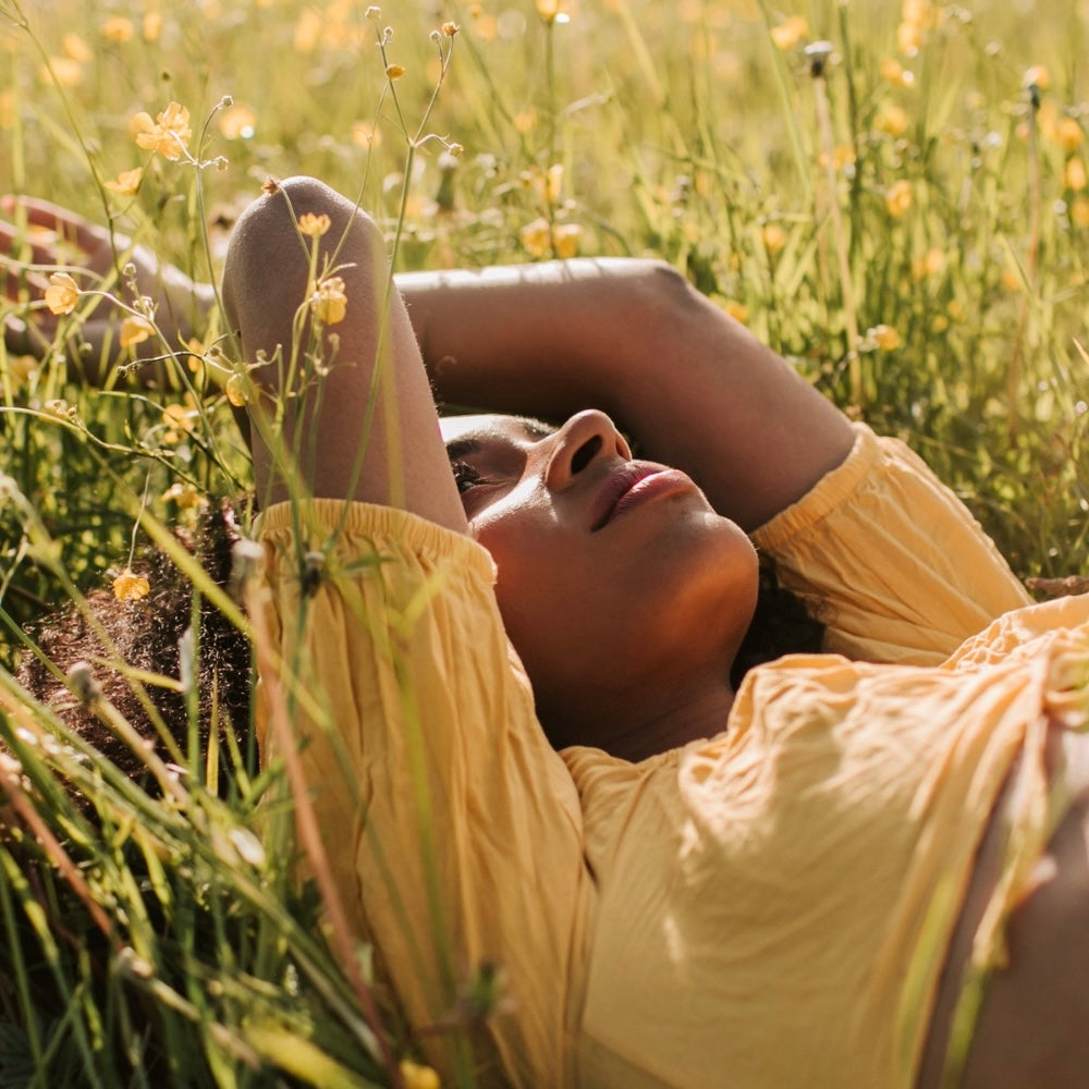Natural Scottish skincare inspired by the landscape, featuring a woman relaxing in a summer meadow.